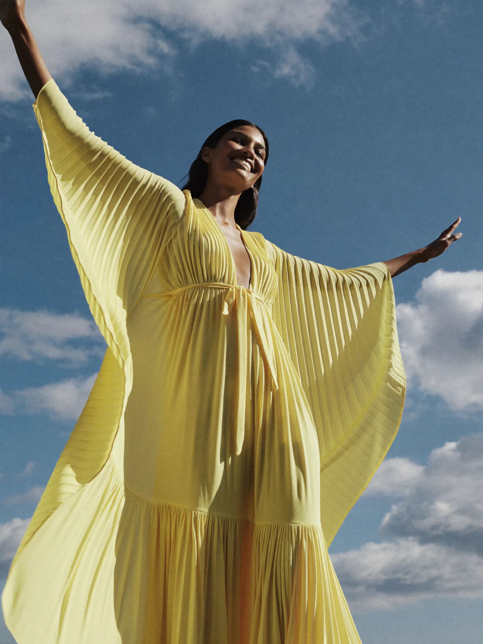 Model in a billowing yellow dress under a blue sky