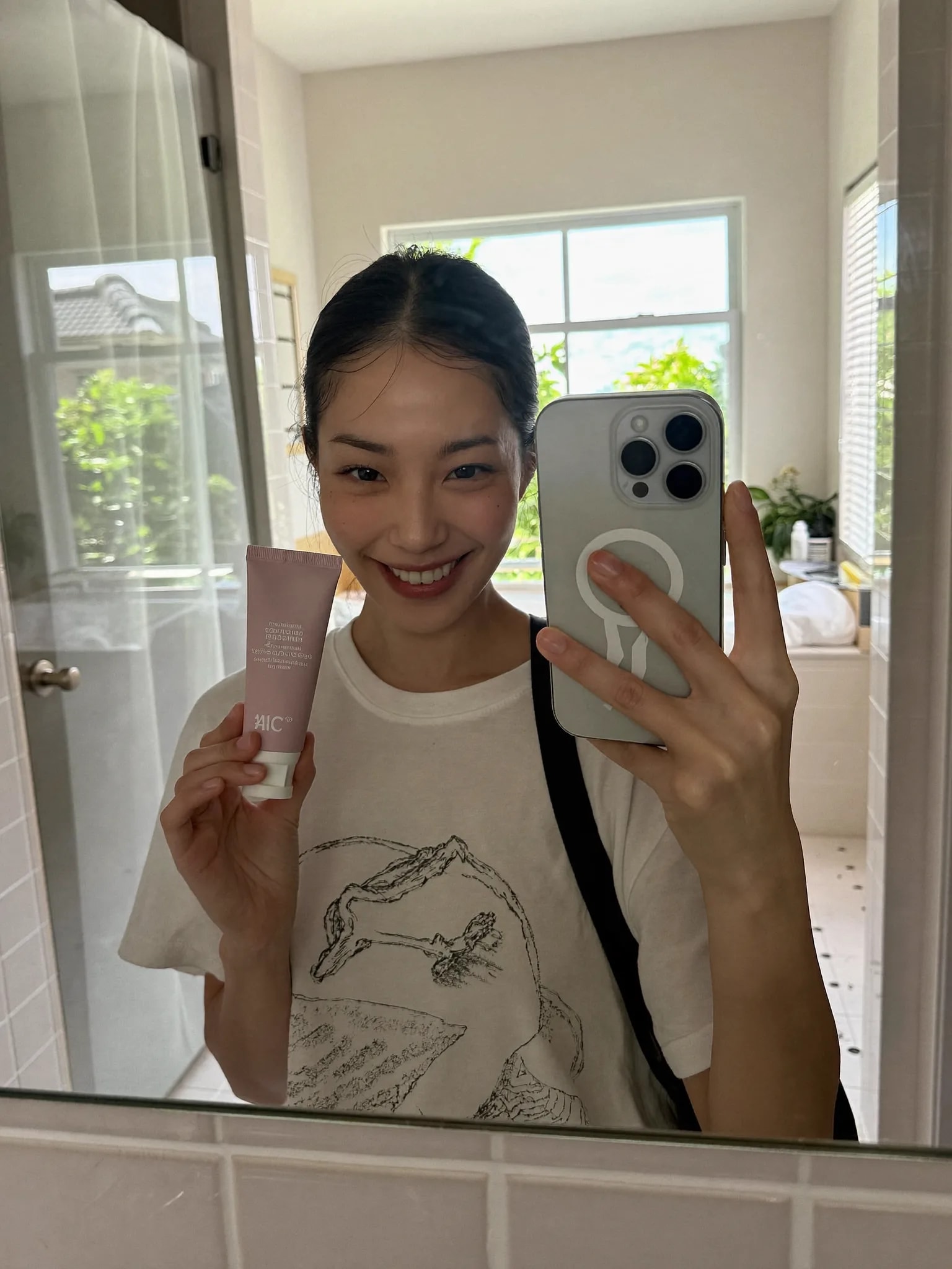 Mirror selfie holding a pink skincare tube